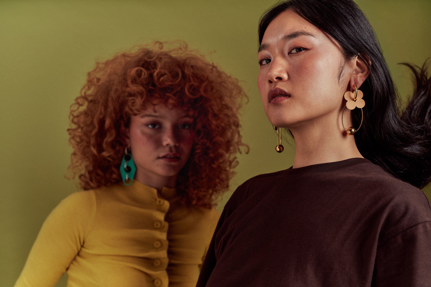 Two models wearing ISLI Studio earrings against an olive green backdrop