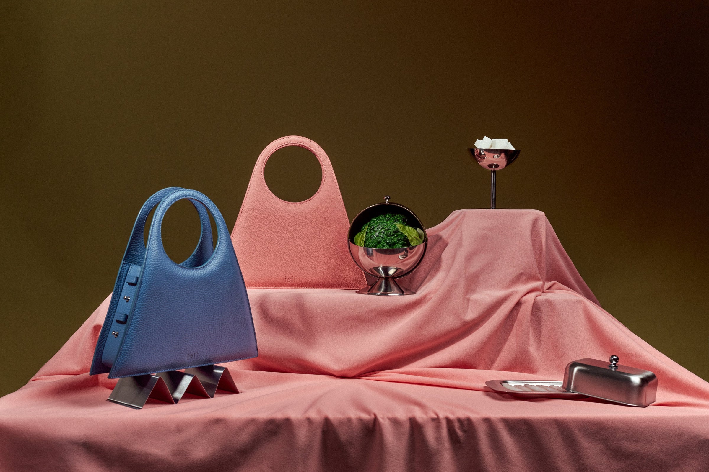 Blue and pink ISLI Studio bags staged on pink drapery against a brown backdrop