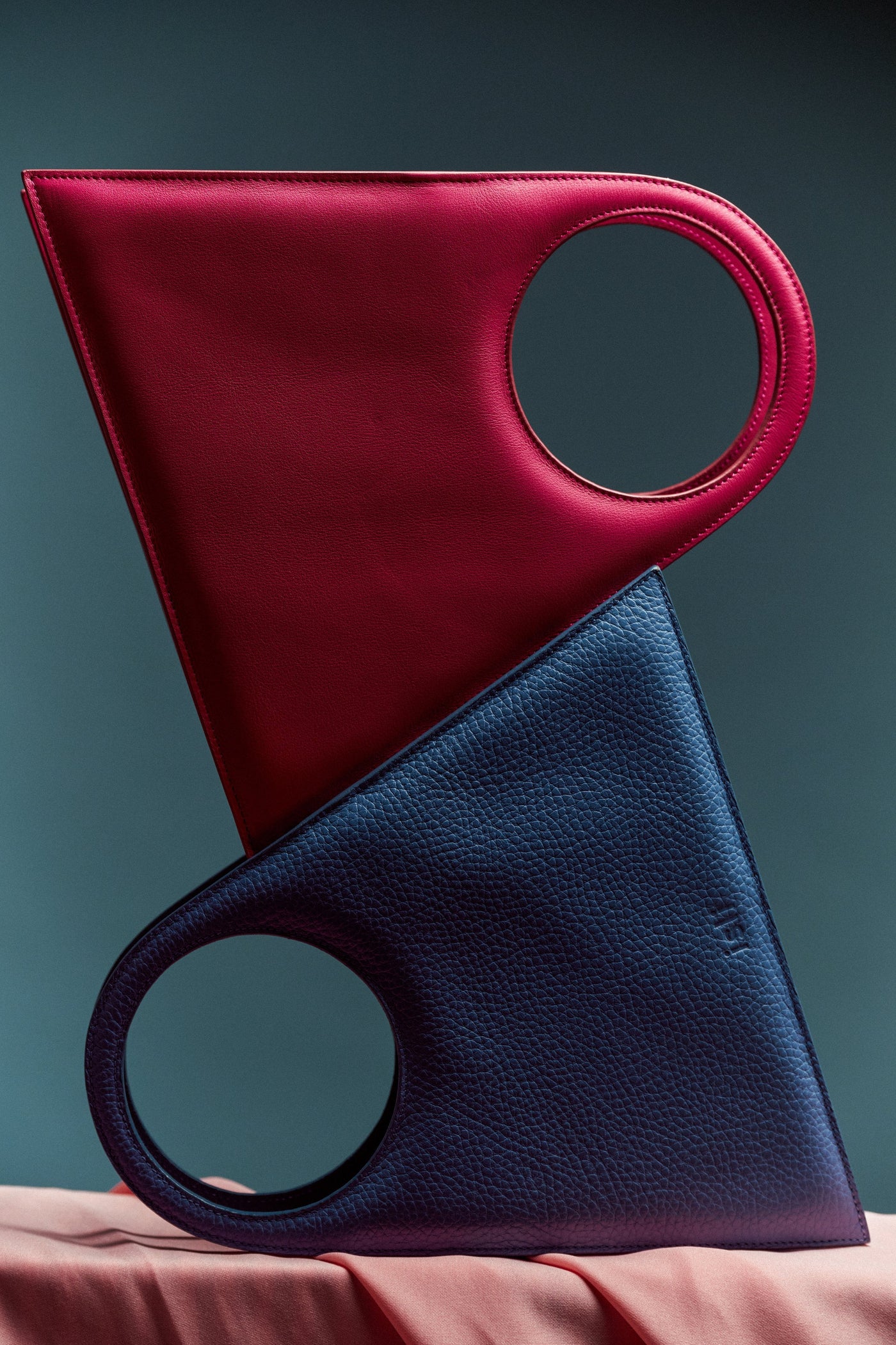 A red and a blue ISLI Studio bag leaning against each other, showing their circular handles