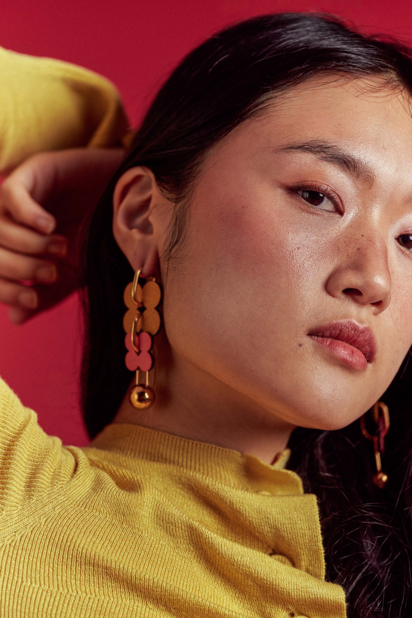 A model wearing gold and pink ISLI Studio drop earrings against a red backdrop