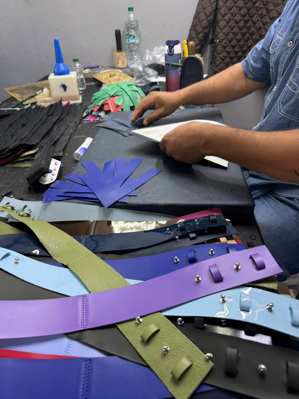 An artisan at the bench, positioning a leather panel among cut straps and tools.