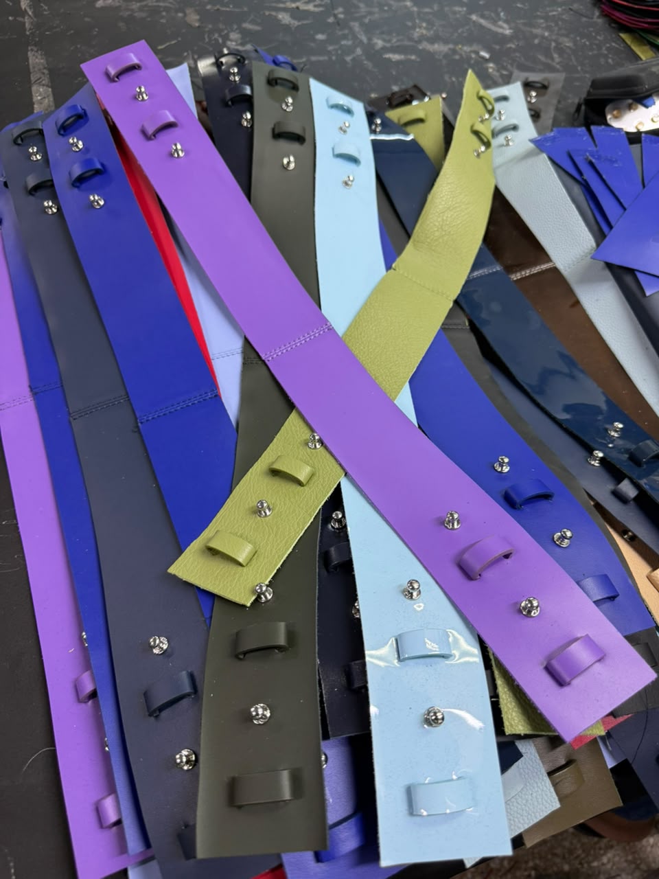 Bag handles in purple, olive, black and pale blue, cut and riveted, spread across the bench.