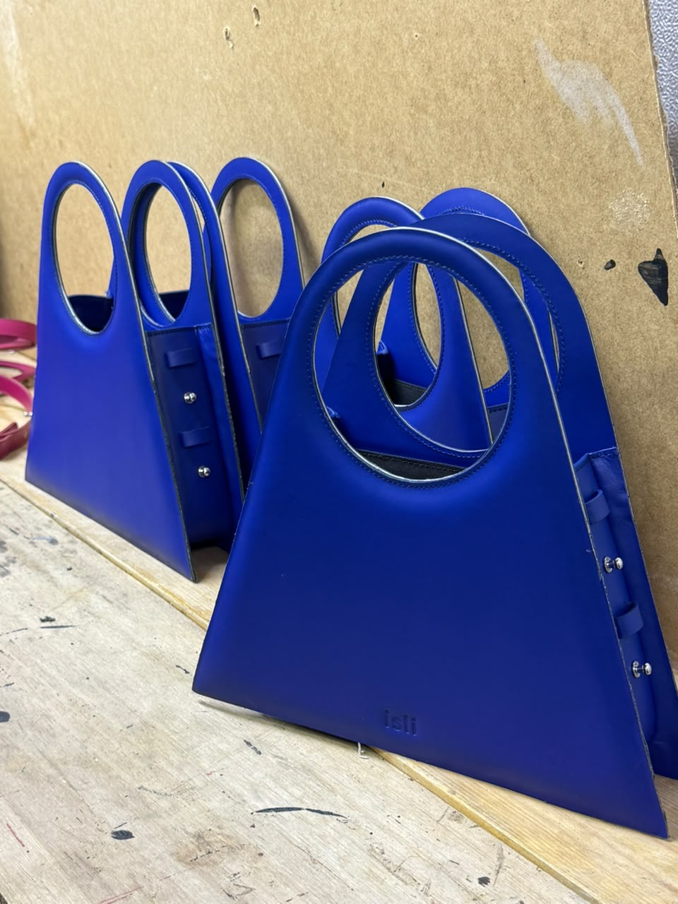 Four electric blue Toubkal bags standing in a row against a cardboard wall.