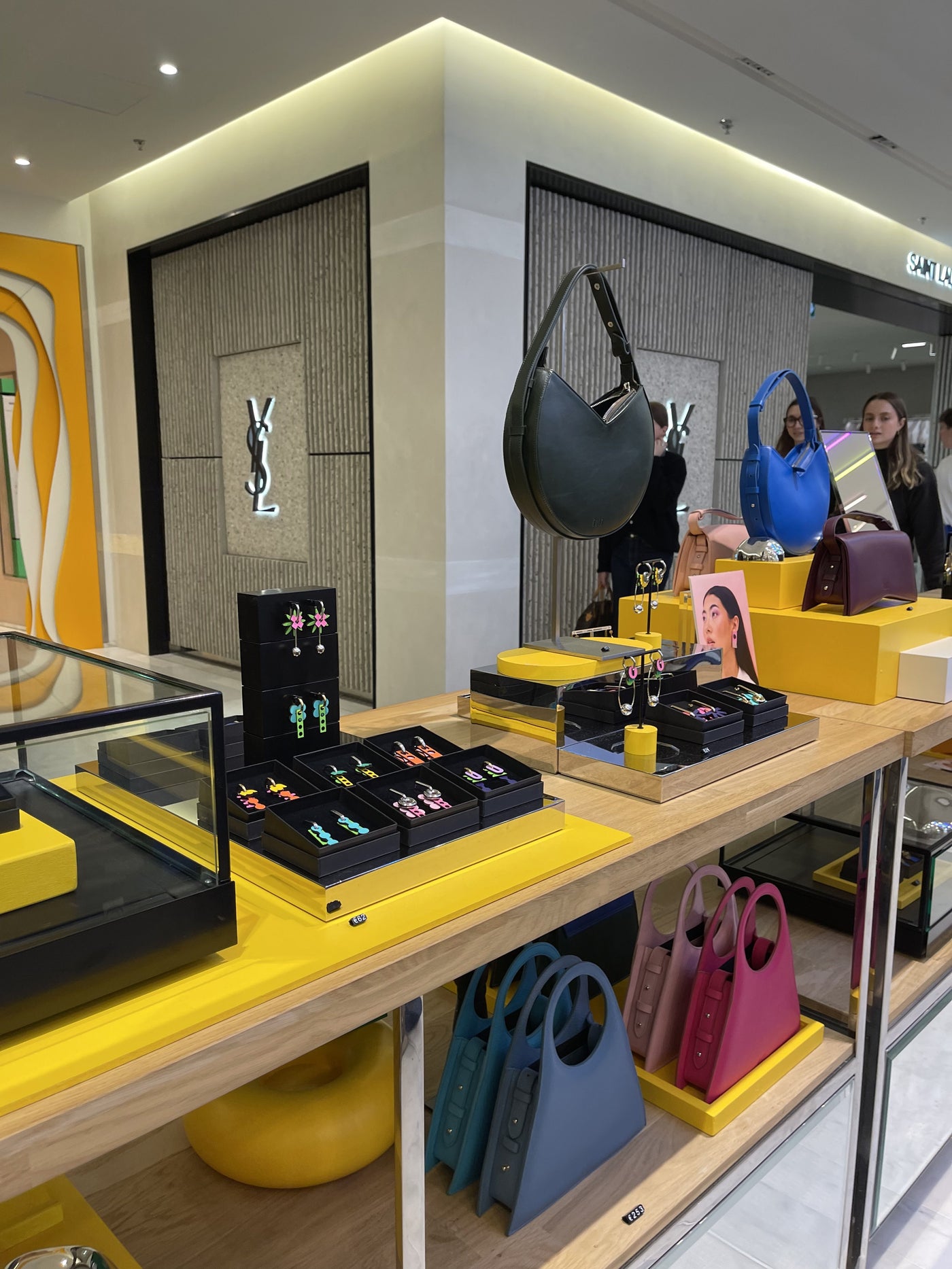 The ISLI stand at Printemps Haussmann in Paris, a wood and yellow display of earrings and bags, with luxury storefronts behind